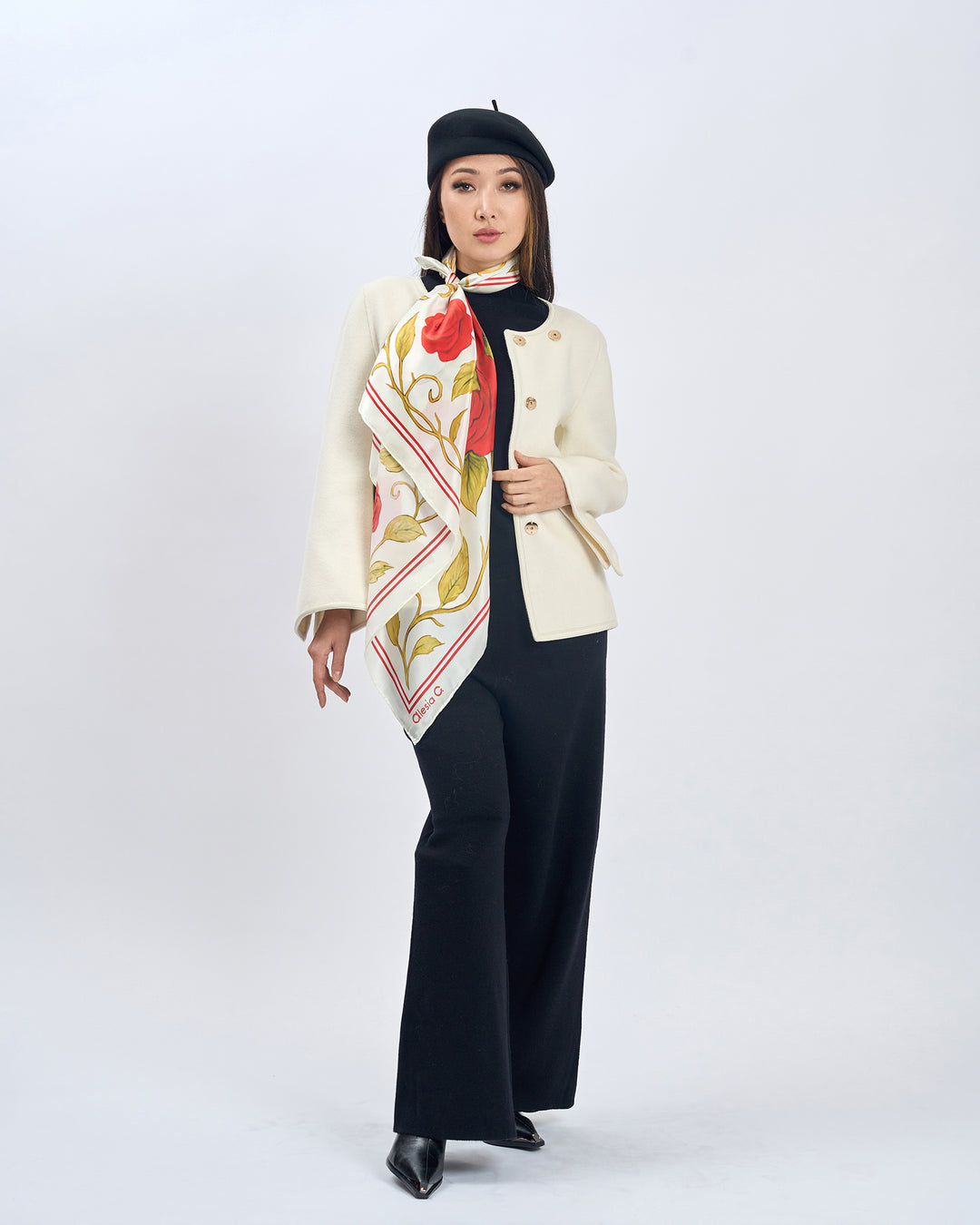Woman wearing a floral scarf, beige coat, black pants, and black beret on a white background.  Red Rose Garden Silk Scarf - Bright Red and Cream Ivory - Alesia C. Floral Collection. AlesiaC.com